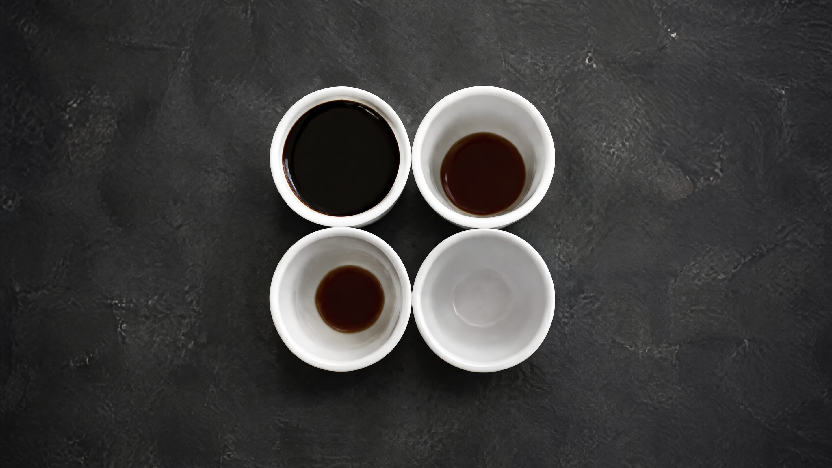 Quatre tasses blanches identiques disposées en carré, vues de dessus, remplies chacune à un niveau différent.